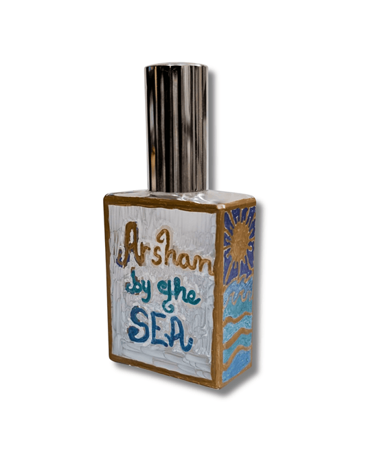 An original hand-painted decorative rectangular bottle with a metallic silver cap, featuring hand-painted artwork on the front and side. The front is painted white with the words 'Arshan by the SEA' in blue and gold lettering, and the side depicts a blue sun and waves with gold accents.
